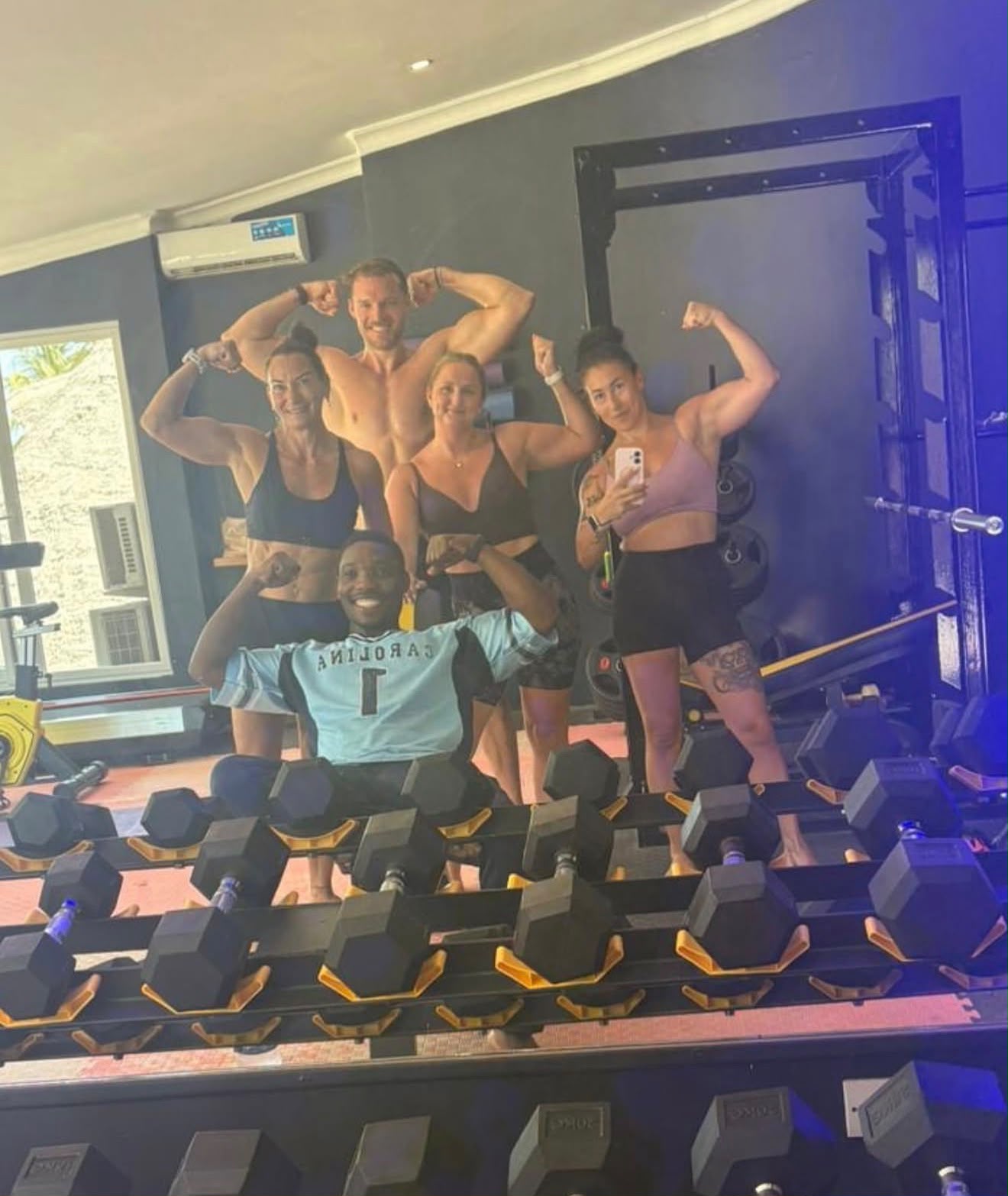 Five members flexing together in front of the dumbbell rack after a session
